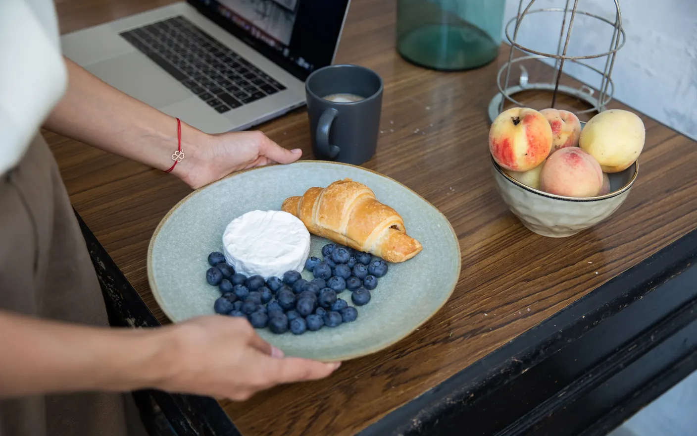 A plate of blueberries, camembert and a croissant with coffee on a desk during a break.